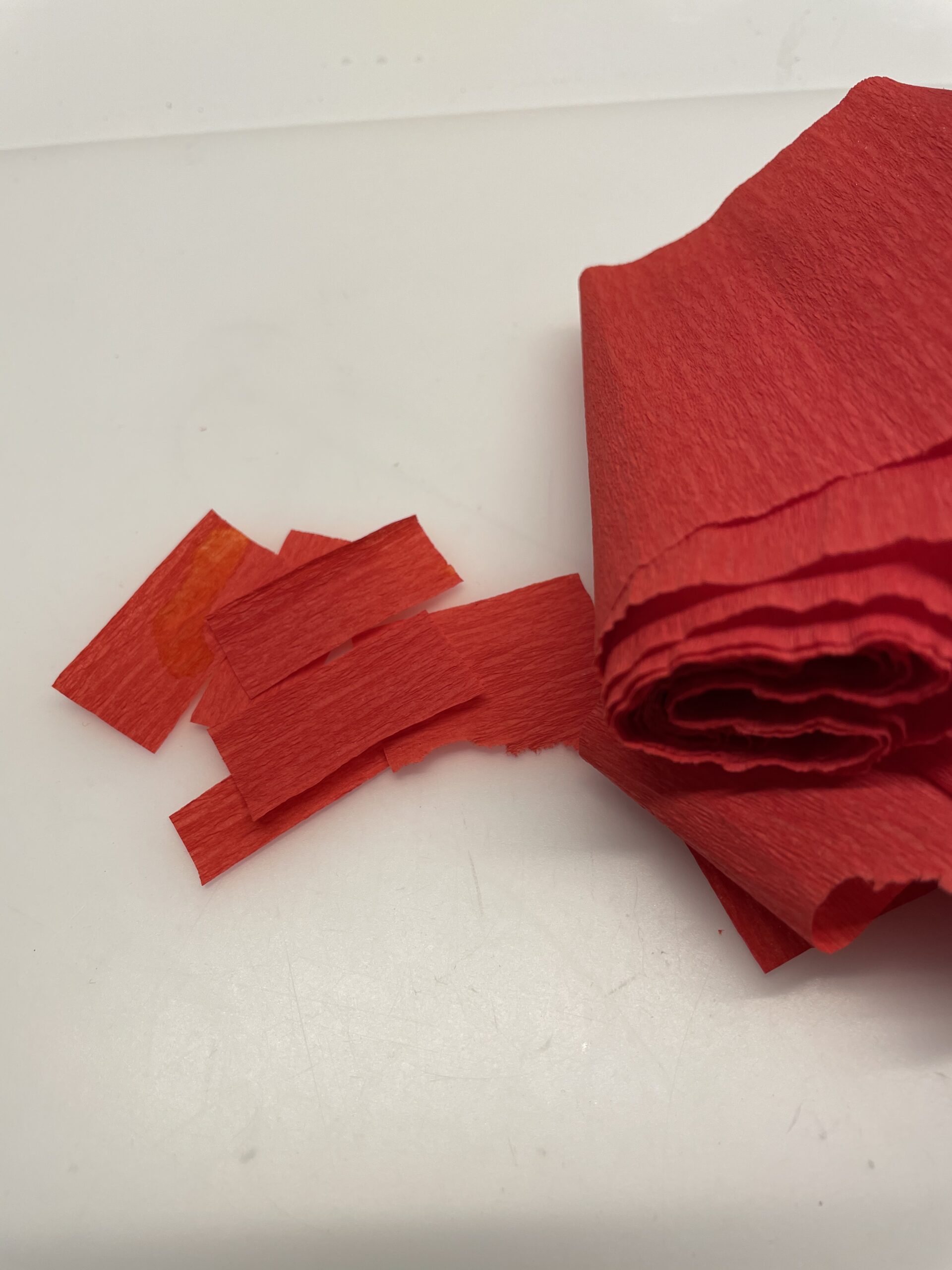 Bild zum Schritt 8 für das Bastel- und DIY-Abenteuer für Kinder: 'Jetzt schneidet ihr euch ein paar Streifen rotes Krepppapier ab.'