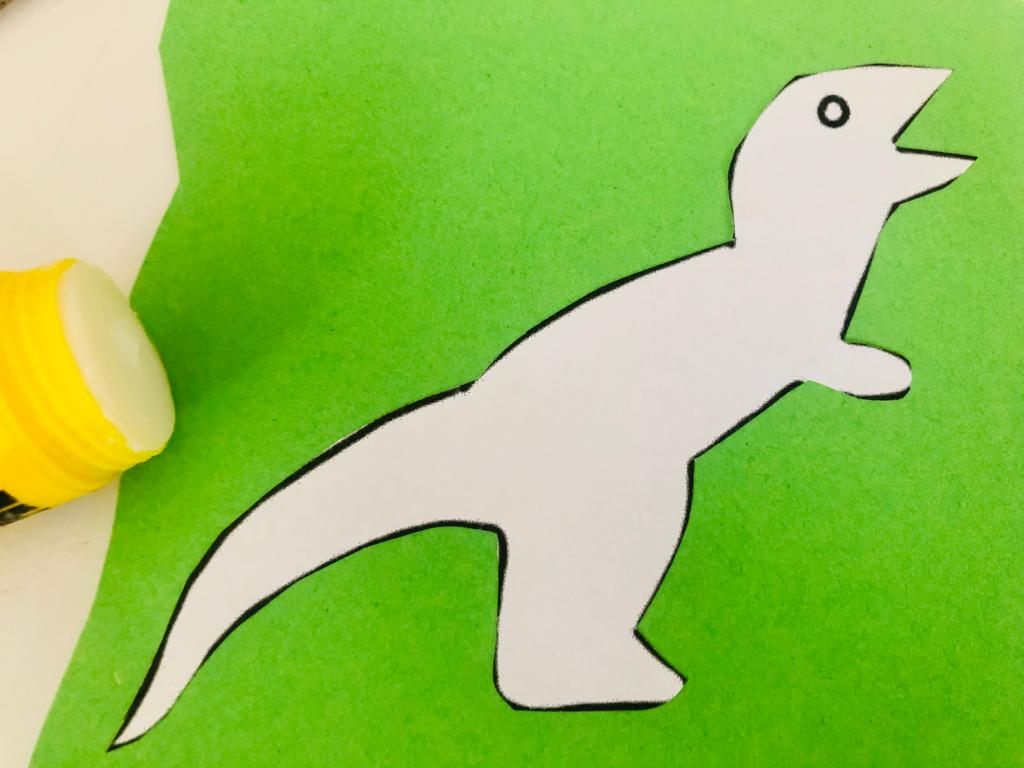 Bild zum Schritt 4 für das Bastel- und DIY-Abenteuer für Kinder: 'Klebt nun den ausgeschnittenen Dino auf ein farbiges Tonpapier.'