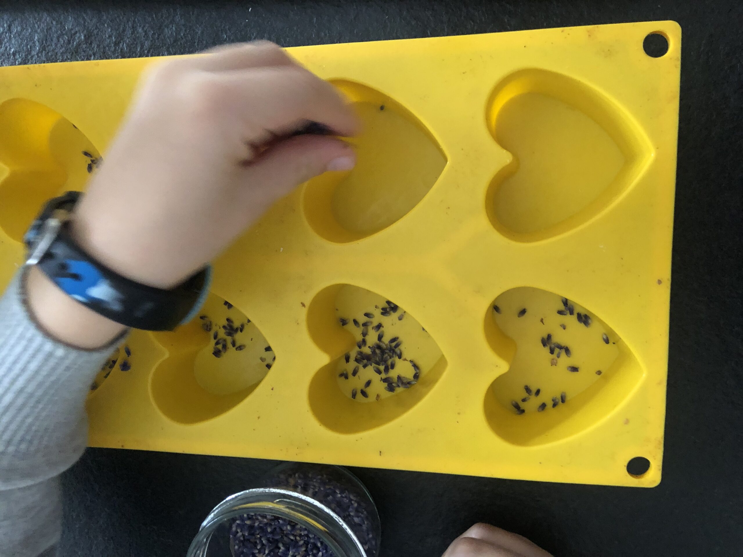 Bild zum Schritt 8 für das Bastel- und DIY-Abenteuer für Kinder: 'Jetzt streut ihr in die Silikonformen etwas getrocknete Lavendelblüten.'
