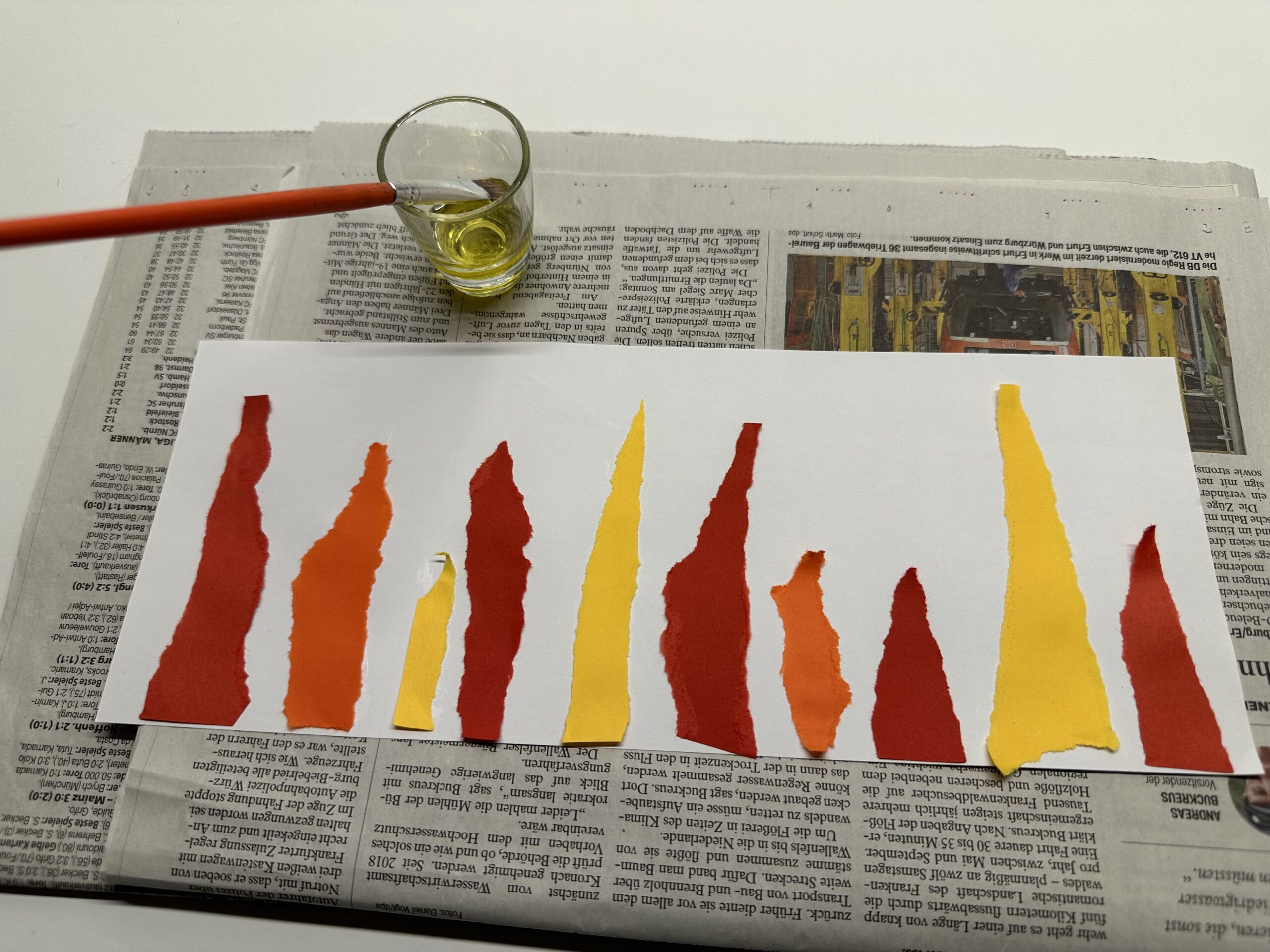 Bild zum Schritt 10 für das Bastel- und DIY-Abenteuer für Kinder: 'Legt das Flammenbild auf ein doppelt gelegtes Zeitungspapier. Stellt ein...'